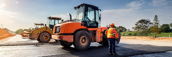 Three construction vehicles line up on a newly paved asphalt road 